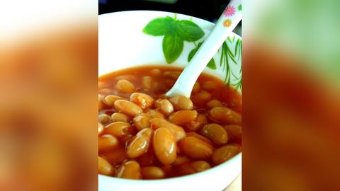 A white bowl of baked beans in tomato sauce with a spoon