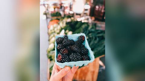 A punnet of blackberries held in a hand at a market