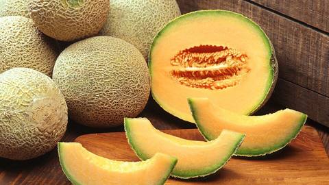 Whole and sliced cantaloupe melons on a wooden table