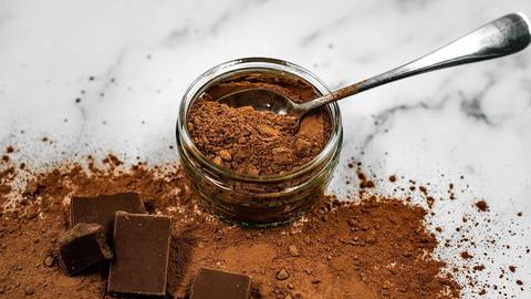 Cocoa powder in a glass jar with chocolate pieces on a marble surface