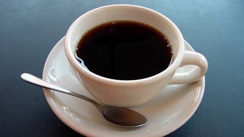 A white cup of black coffee on a saucer with a spoon