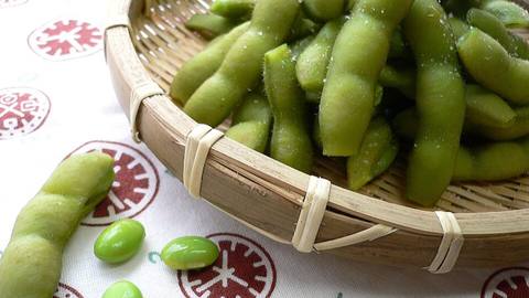 Edamame pods in a woven basket with shelled beans in front