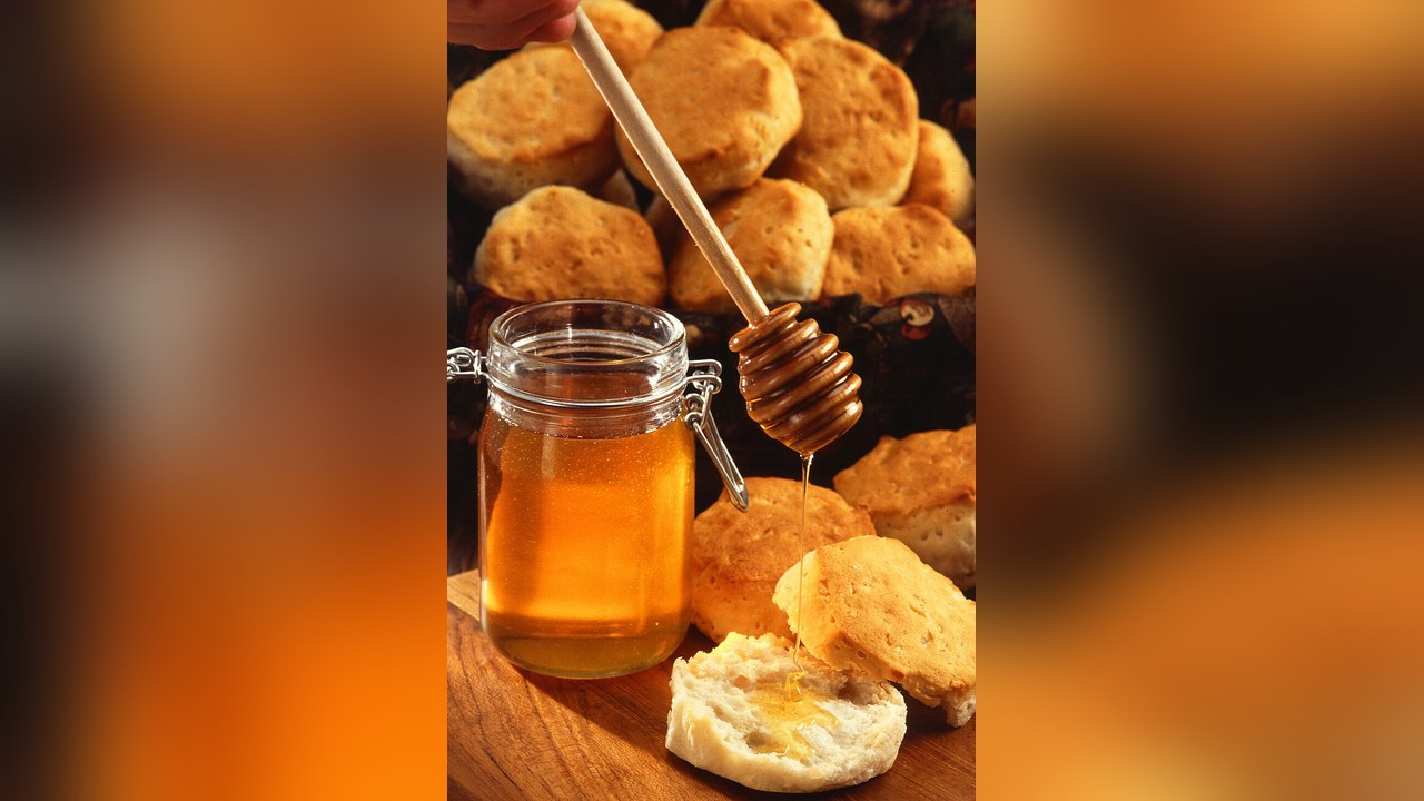 A jar of honey with a honey dipper beside scones