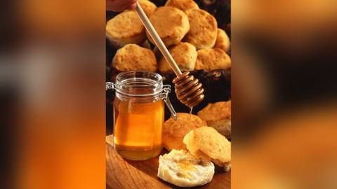 A jar of honey with a honey dipper beside scones