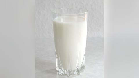 A glass of milk against a plain wall
