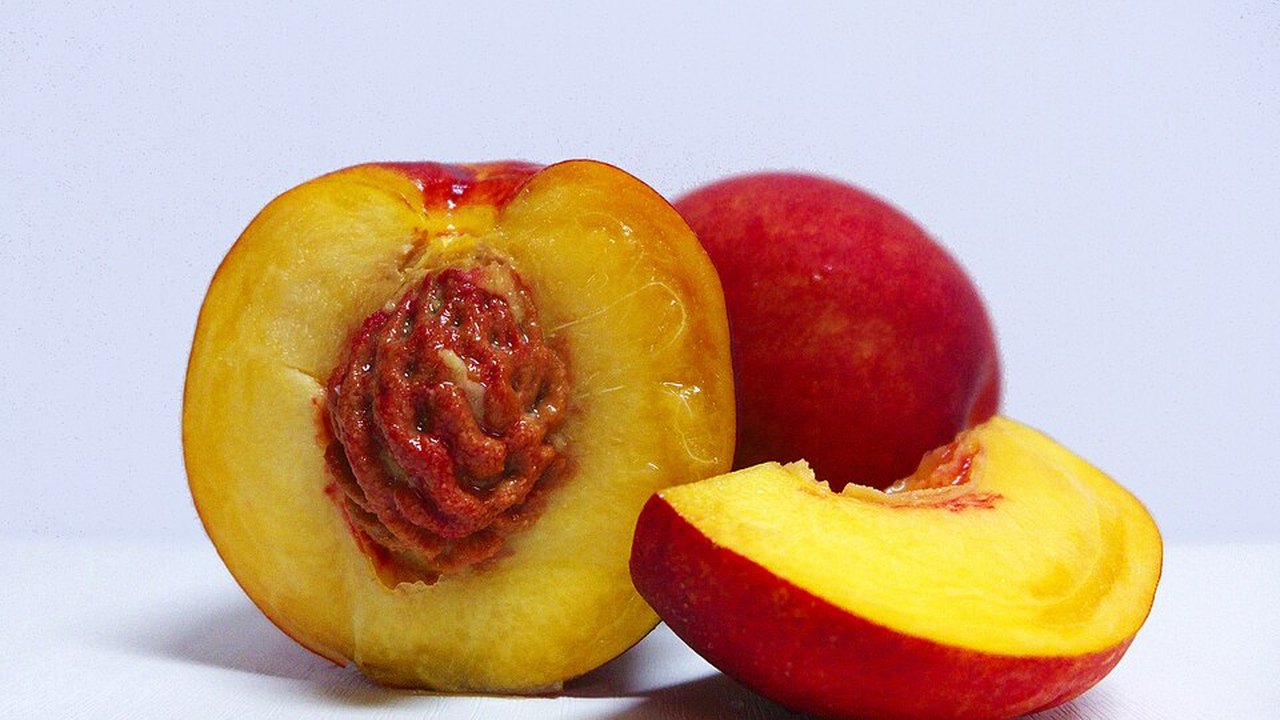 A halved nectarine showing the stone beside a whole one