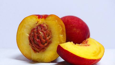 A halved nectarine showing the stone beside a whole one