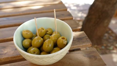 A bowl of green olives with cocktail sticks on a wooden table