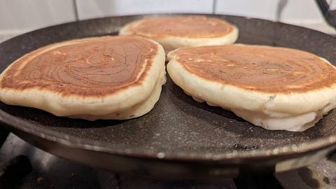 Pancakes cooking on a dark griddle