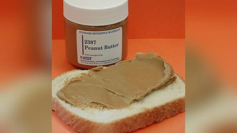 A jar of peanut butter beside a slice of bread spread with it
