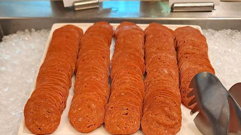 Slices of pepperoni laid out in rows on ice with a pair of tongs