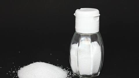 A shaker of salt and a small pile of salt crystals