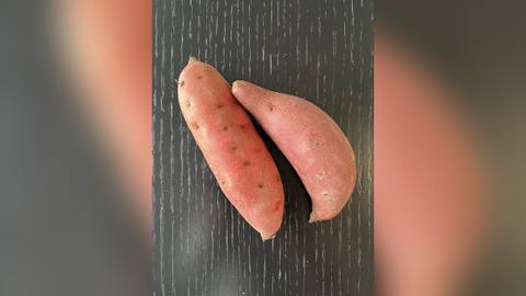 Two sweet potatoes on a dark wooden surface