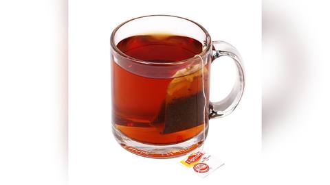 A glass mug of black tea with a teabag in it
