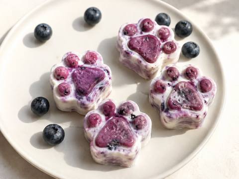 Frozen blueberry and yogurt dog treats shaped like small paw prints on a white plate