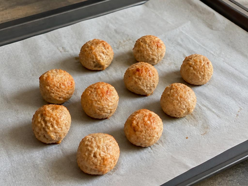 Pequeñas albóndigas de pavo y calabaza cocidas, en una bandeja de horno forrada con papel de horno, sin salsa ni guarnición.