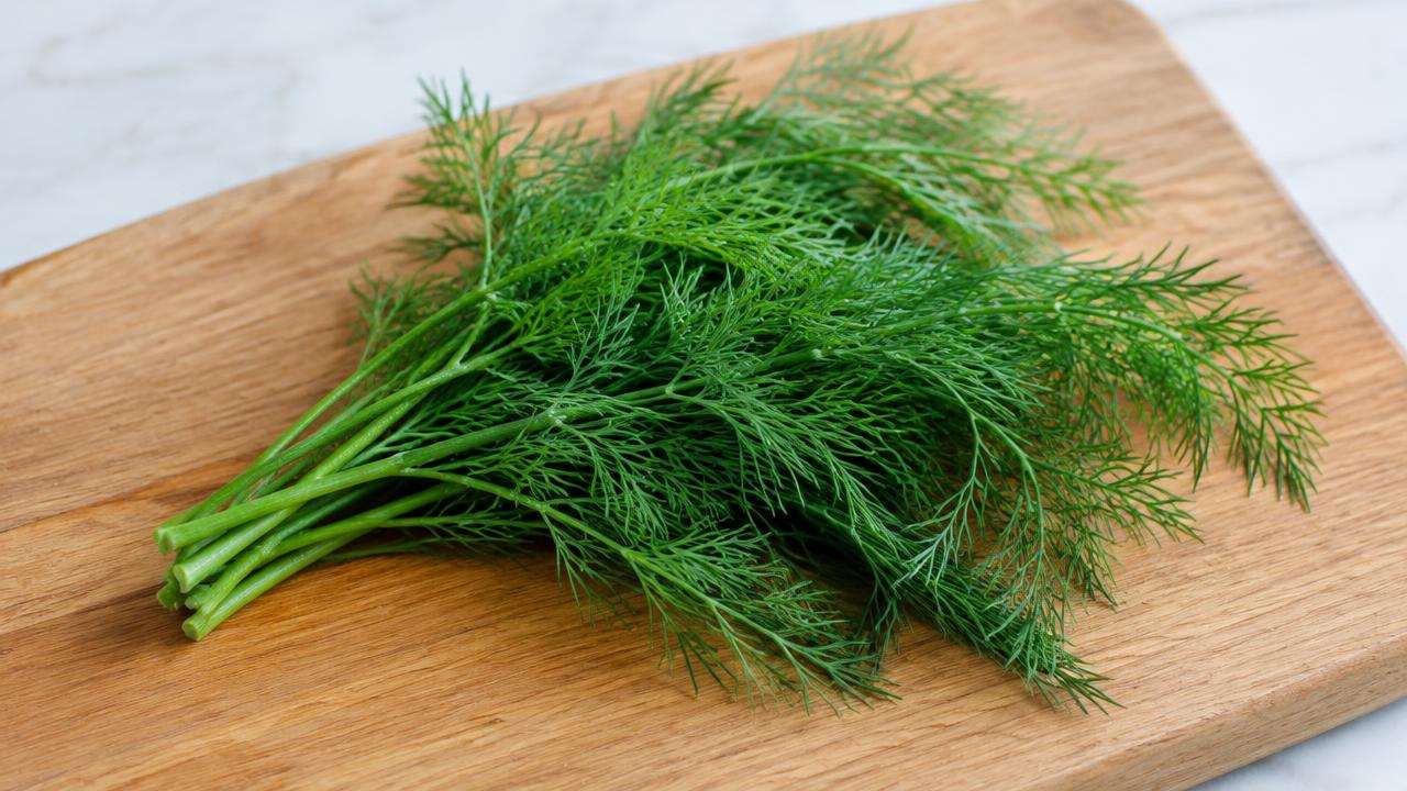 A small bunch of fresh green dill sprigs on a wooden chopping board.