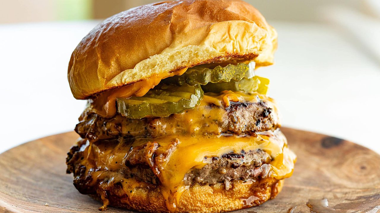 A double cheeseburger with pickles on a wooden plate