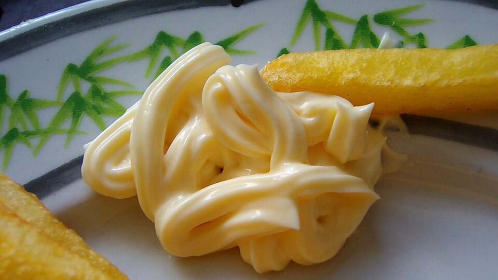 A swirl of mayonnaise on a plate next to a piece of fried potato