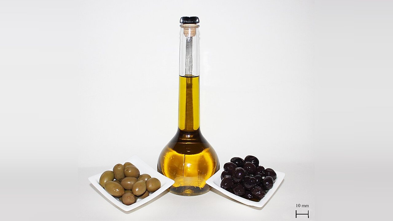 A bottle of olive oil with small bowls of green and black olives