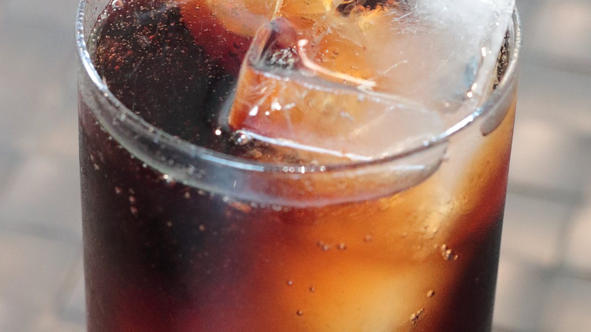A tall glass of cola with ice and a lemon slice