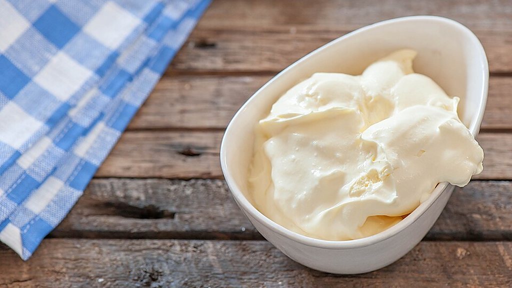 Sour cream in a white dish on a wooden table with a blue checked cloth