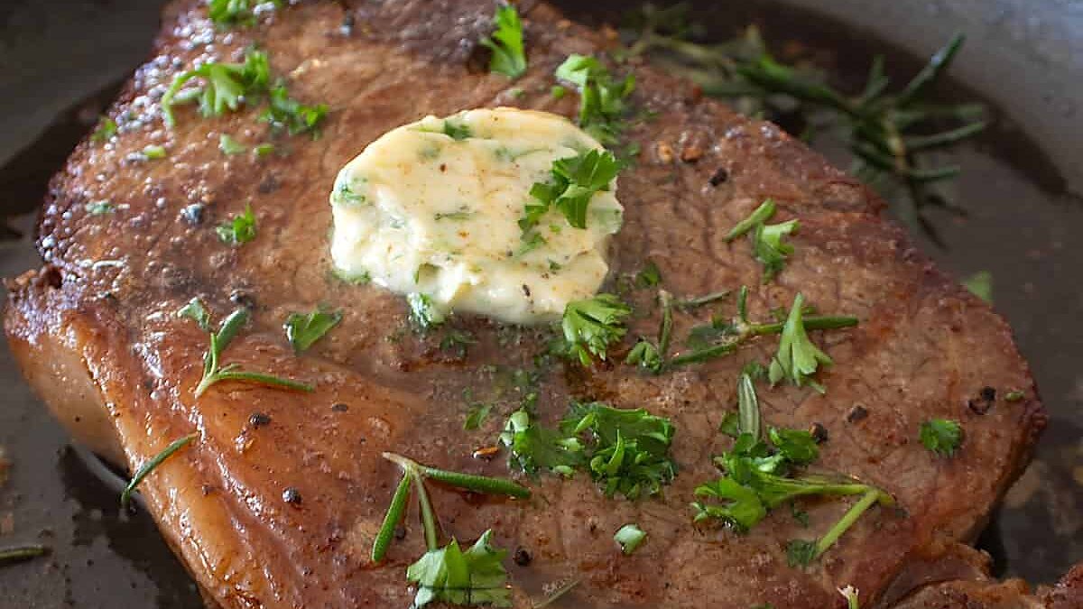 A pan-seared steak topped with herb butter and chopped herbs