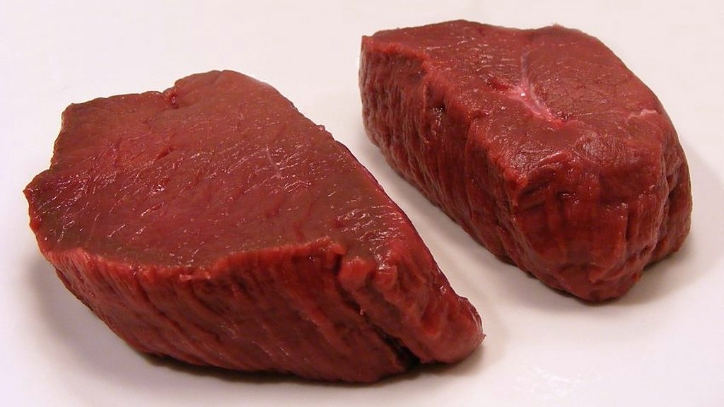 Two raw venison steaks on a white plate