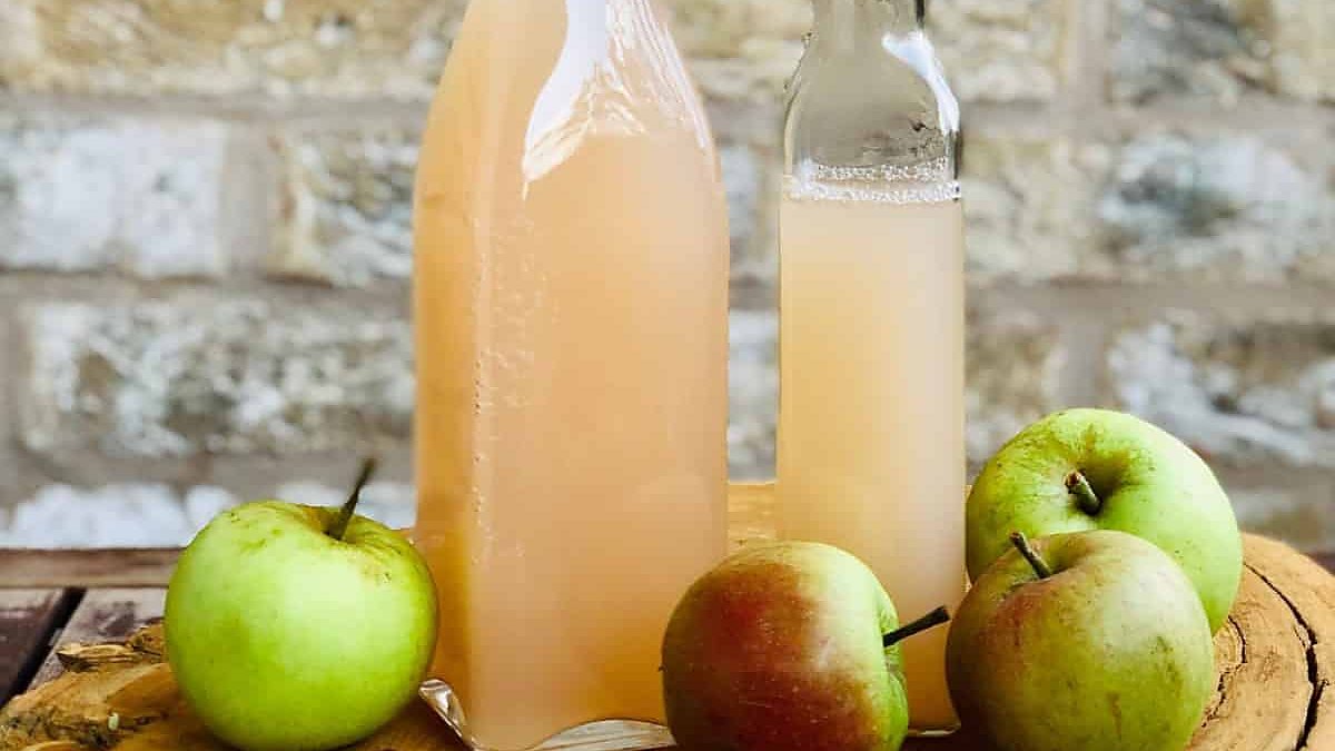Two bottles of apple cider vinegar with fresh apples on a wooden board